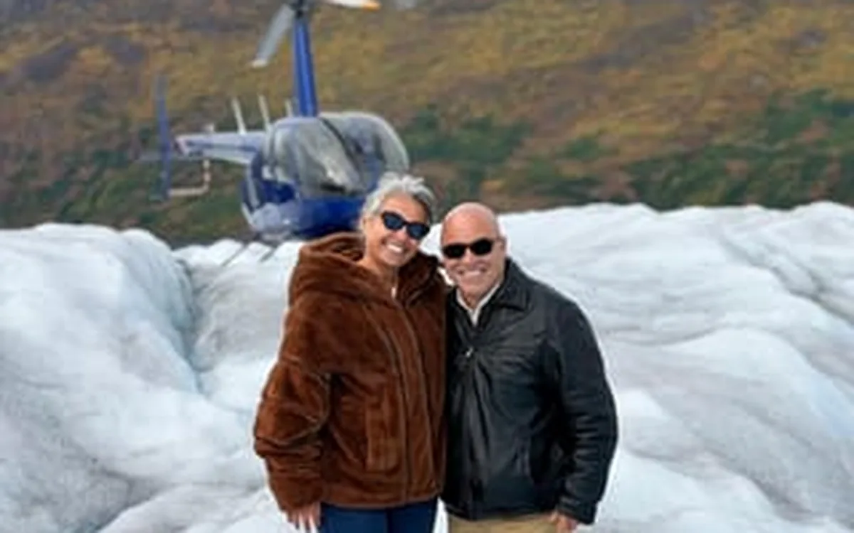 Two people standing on glacier ice beside a helicopter in Alaska