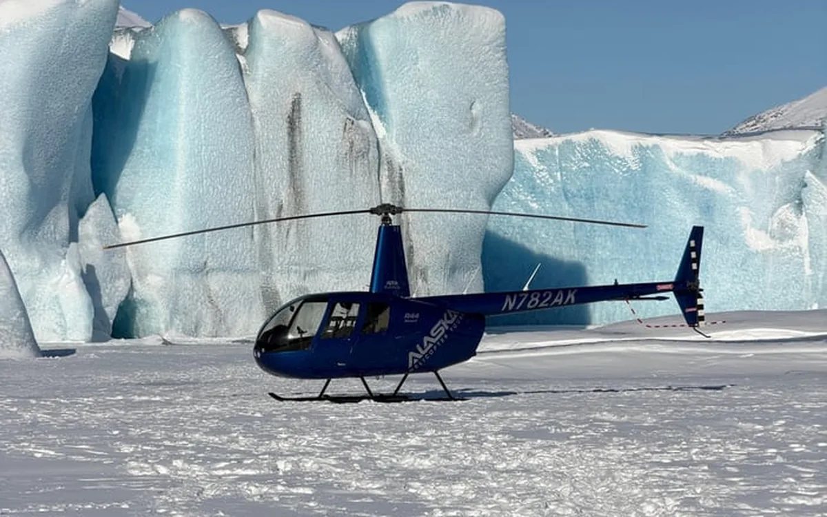 A helicopter parked on the ice in front of a wall of blue seracs, Alaska