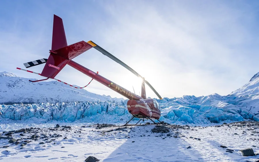 A red helicopter on blue glacier ice under mountains in Alaska