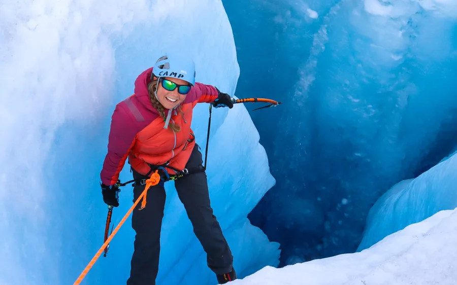 A climber on a blue ice wall inside a glacier crevasse in Alaska