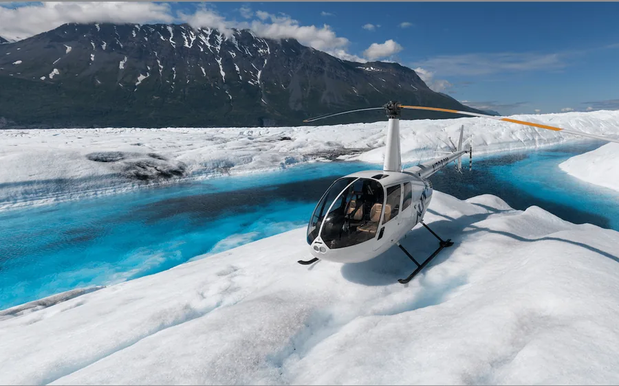 A helicopter on Knik Glacier beside a turquoise meltwater lake, Alaska
