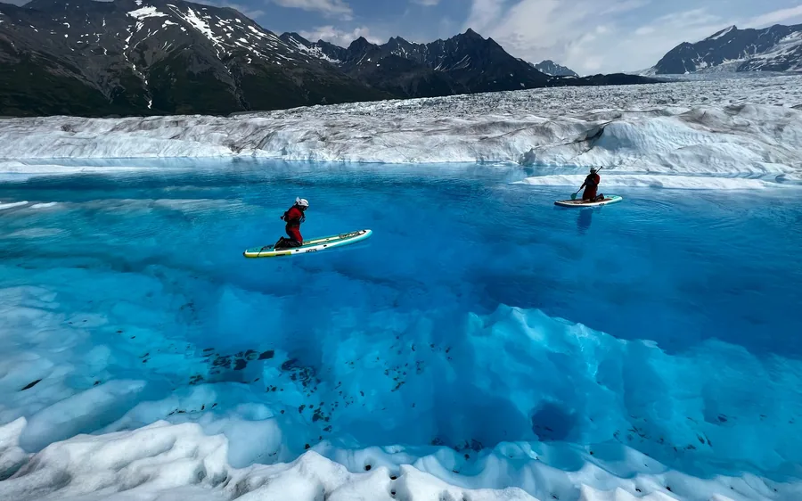 A paddleboarder on a turquoise glacial lake beside icebergs in Alaska